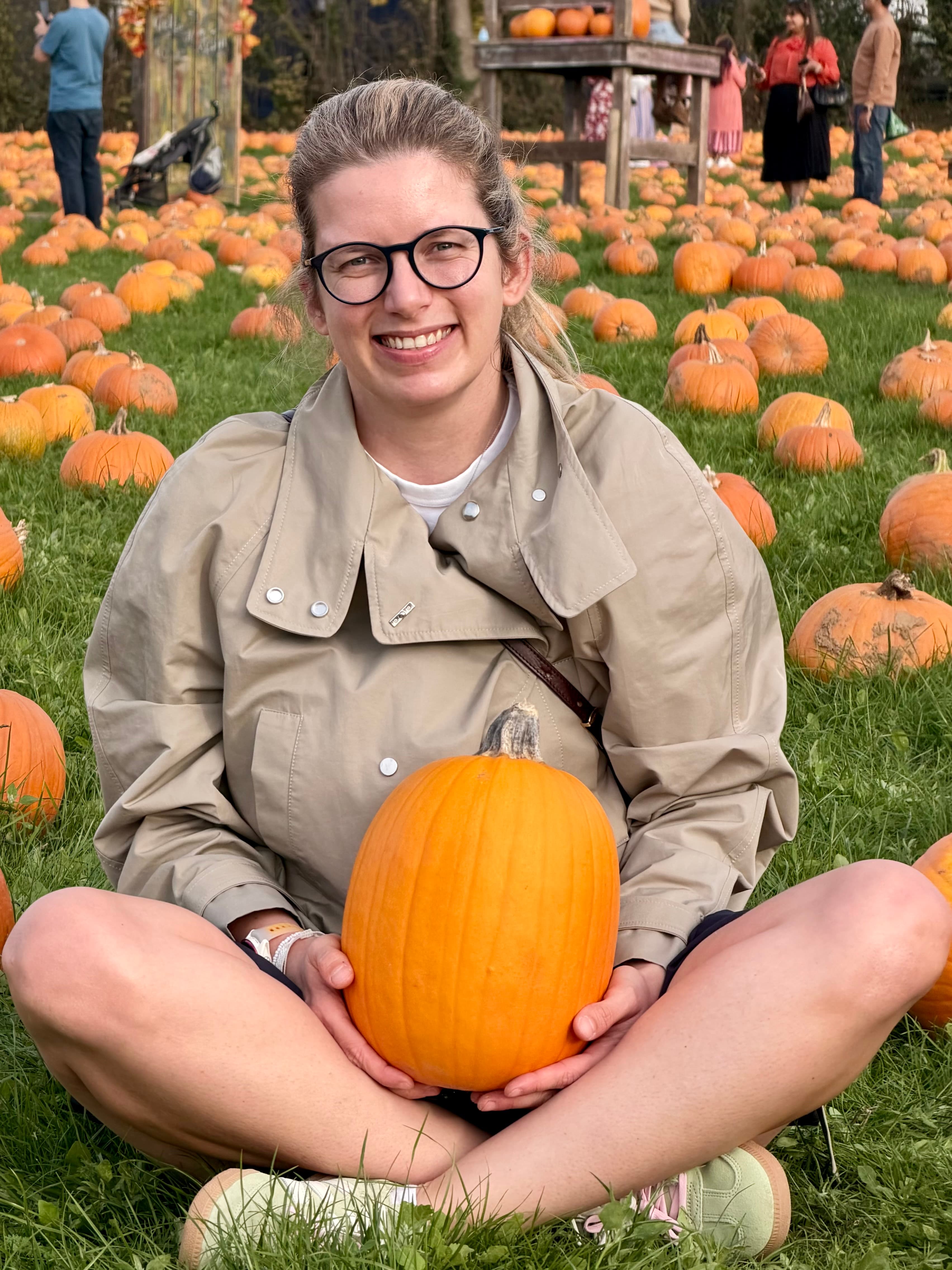 Sitting cross-legged in the field holding a tall pumpkin